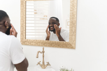 Black happy man washes his face in the bathroom. Daily routine