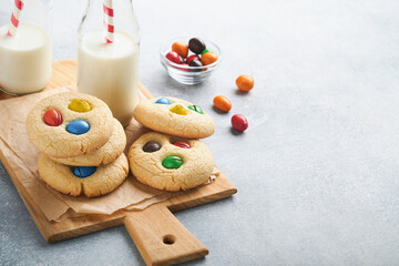 Obraz na płótnie Canvas Homemade cookies with colorful chocolate candies and milk. Stack of shortbread cookies with multi colored candy on plate with bottle of milk on light gray background. Baby food concept. Copy space.