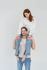 Cheerful man holding barefoot girlfriend on shoulders isolated on white.