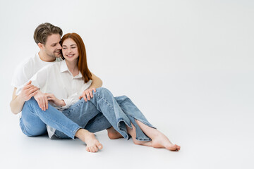 Smiling man in jeans kissing girlfriend in shirt on white background.