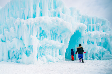 Two children bundled up in winter gear run into a blue tinged frozen ice castle