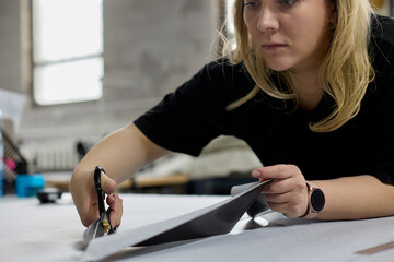 Close-up of dressmaker cutting piece of fabric with scissors in sewing workshop. Process of manufacturing a piece of clothing or upholstery for upholstered furniture made of fabric in studio workshop