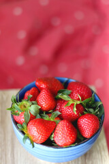 Bowl of fresh strawberries. Red bedding in the background. Selective focus.