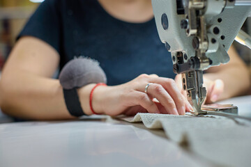 Close up view of sewing process. Female hands stitching white fabric on professional manufacturing...