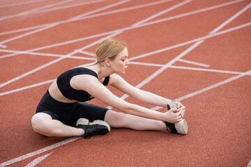 full length view of sportswoman stretching while sitting on stadium.