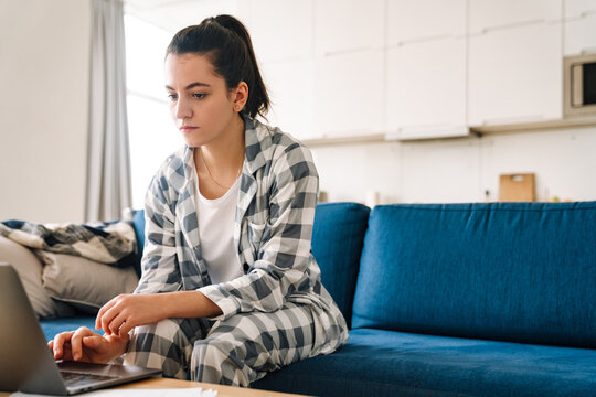 Young woman wearing pajama using laptop while sitting on couch