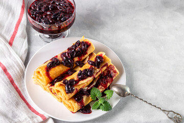 Rolled pancakes with honeysuckle jam on a plate with a mint leaf. Copy space