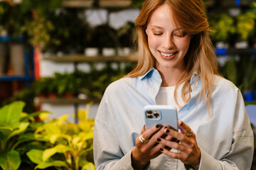 White young florist girl smiling and using cellphone in flower shop