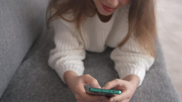 Close-up of female hands with a modern smartphone. In the background, a blurry part of a woman's smiling face can be seen.