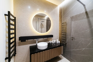 Stylish interior design in the bathroom with round mirror and black countertop