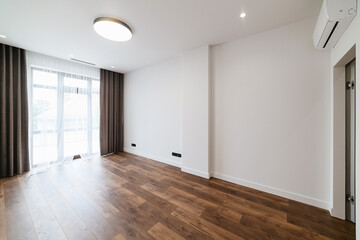 Large, new, empty room with white walls and wood floors. Large window in the room