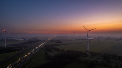 Aerial view sunrise of meadows and electric windmills across high speed highway on the morning under a colorful sky natural landscape over the panorama landscape. High quality photo