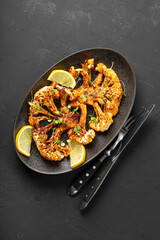 Vegetarian cauliflower steaks with microgreens and lemon on the black background, top view vertical photo. Alternative to traditional meat steaks for vegans.