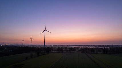 Obraz premium Silhouette of Wind turbines field against sunrise or sunset sky background. Windmill, eco power. Green energy technology concept. High quality photo