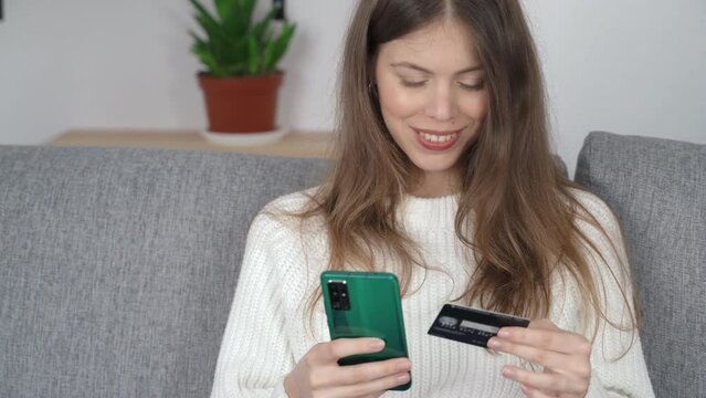 A young girl sits with a phone in one hand and a bank card in the other. Online shopping concept.