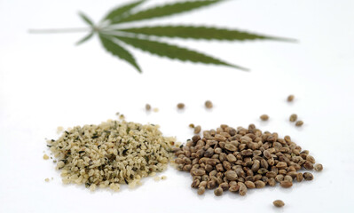 Two heaps of raw hemp seeds, whole and shelled, and cannabis leaf on a white background. Selective focus.