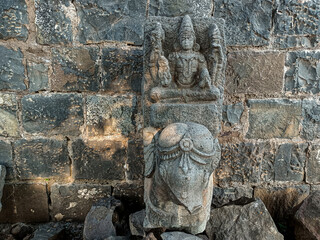 Stock photo of ruined ancient sculpture of Hindu trinity god sitting on elephant, idol carved out off gary color granite sunlight falling on idol, Picture captured at Khidrapur, Maharashtra, India.