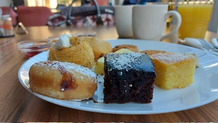 Kanafeh-Kuchen. Dessert auf einem weißen Porzellanteller. Orientalische Kekse. Schokoladenwürfel mit Kokos. Kadaif mit Walnüssen. Donuts. Sesamkuchen. Gläser mit Fruchtmarmelade.