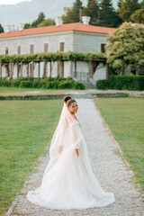 Fototapeta premium Portrait of the bride in a cream dress on the background of a luxurious mansion.