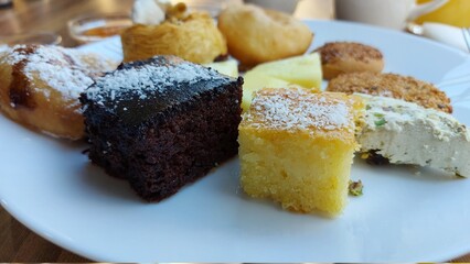 Dessert auf einem weißen Porzellanteller. Orientalische Kekse. Schokoladenwürfel mit Kokos. Kadaif mit Walnüssen. Donuts. Sesamkuchen. Gläser mit Fruchtmarmelade. Kanafeh-Kuchen.