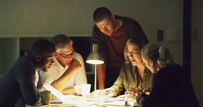 Working late but working hard as a goal-oriented team. A group of businesspeople working late in an office. Diverse group of serious colleagues brainstorming together late at night, talking.