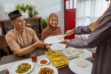 Fototapeta na wymiar excited asian muslim woman served the food for friend while sitting on dining table for iftar or eid mubarak gathering at home