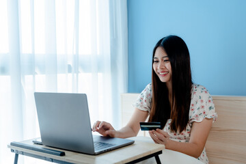  Beautiful Asian girl, Shopping online via laptop computer, sitting happily looking at credit card when the credit card payment is successful, online shopping..