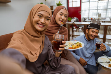 asian muslim friend take selfie together with smartphone while having iftar dinner together