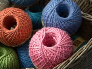Focus on a pink ball of gardeners twine amongst other coloured balls in a wicker basket.