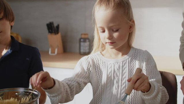 Cute son and daughter learn how to cook omlet, having fun, helping parents in kitchen. Caucasian family with little kids prepare breakfast together at home.