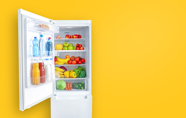 Open fridge full of vegetables, fruits and drinks on yellow wall background. Copy space