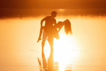 Silhouette of a couple in love, dances with splashes in the water of the lake in the orange sunset