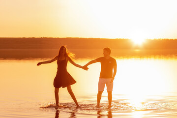 Silhouette of a couple in love, dances with splashes in the water of the lake in the orange sunset