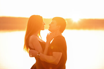 Close-up portrait of a silhouette of a loving couple in the rays of orange sunset. Lovers hug, kiss