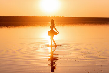 Silhouette of a contempo dancer in black dress in the water of the sea with reflection of the sky