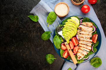 Grilled chicken breast and fresh vegetable salad with spinach leaves, avocado and tomatoes on a dark background. Healthy lifestyle. Ketogenic diet. The concept of diet food. Copy space