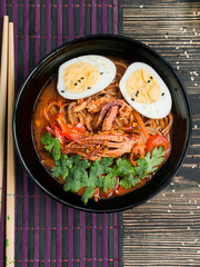 Asian noodle soup, ramen with squid, vegetables, herbs and egg in a black bowl. Top view. Culinary background for recipes. Cook. Food background. Copy space. Table background menu.