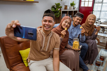 portrait of beautiful muslim friend and family taking their photo together using smartphone while sitting on a sofa at the livingroom during eid mubarak