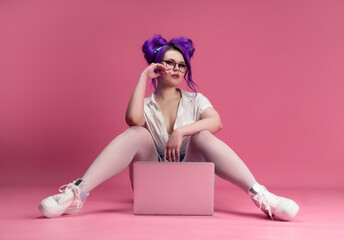 sexy girl with glasses and purple hair with a laptop on a pink background