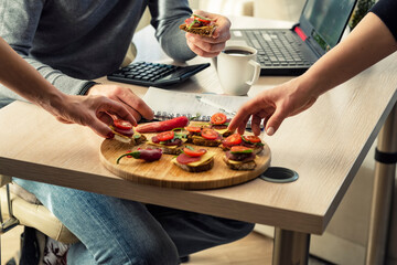 Several workers or students have a snack at the workplace. Hands with sandwiches close up over a desktop with a computer.snacks on sandwiches while working at the workplace. The student has a snack 