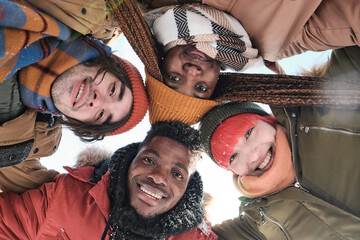 From below view of young African American and Caucasian friends spending snowy winter day together smiling at camera