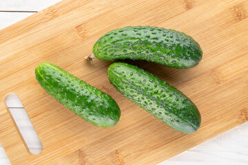 Three organic cucumbers on a cutting board on a wooden table, macro, top view.