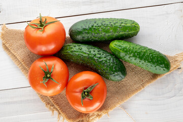 Three organic tomatoes and three cucumbers with a jute napkin on a wooden table, macro, top view.