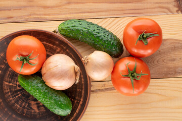 Three organic tomatoes and three cucumbers and two onions with a clay plate on a wooden table, macro, top view.
