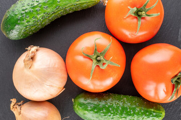Three organic tomatoes, two bulbs and two cucumbers on a slate stone, macro, top view.