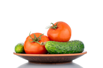 Fototapeta na wymiar Two ripe tomatoes and two cucumbers on a clay plate, macro, isolated on a white background.