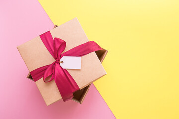 gift box with satin bow and blank tag on yellow and pink background with copy space