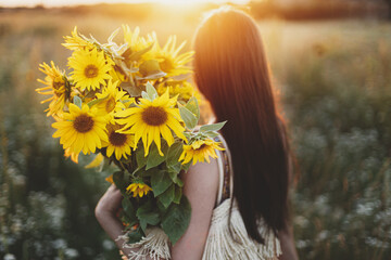 Beautiful woman holding sunflowers bouquet close up in warm sunset light in summer meadow. Tranquil...