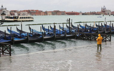 venice at high tide and mooring gondolas with a person in yellow raincoat and rubber boots