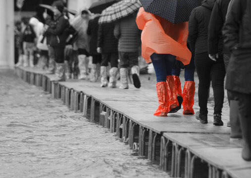 Italy Venice at high tide and people walking over the walkway and red spats and orange raincoat while the rest is black and white